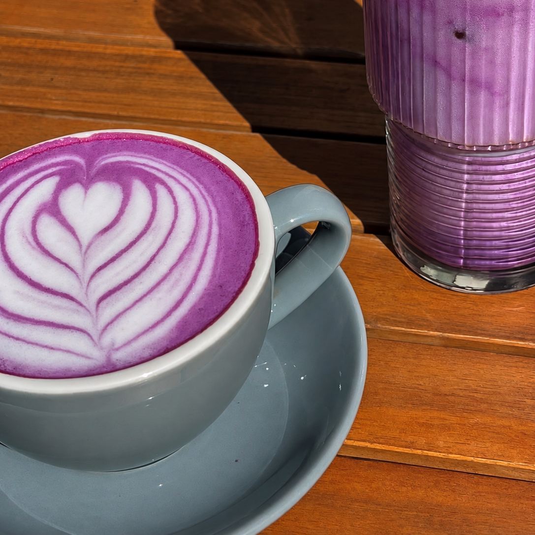 Ube latte met latte art naast een iced ube latte op een tafel in een koffiebar