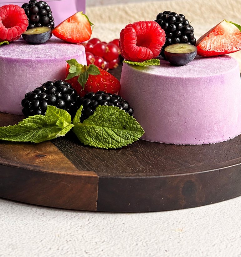 Zwei lila Ube Panna Cotta auf einem Holzbrett mit Himbeeren, Brombeeren, Erdbeeren und Minze